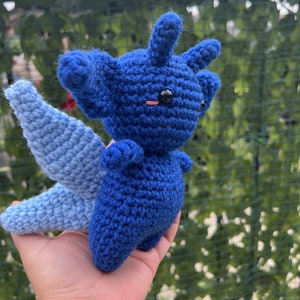 May include: A blue and light blue crocheted stuffed animal with a wing. The animal has a black eye and a pink blush.