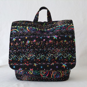 May include: Black quilted backpack with a colorful design featuring stars, confetti, and musical notes. The backpack has a single top handle.