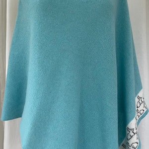 May include: A light blue knitted poncho with a white and grey patterned border.