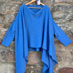 May include: A blue knitted jumper with a draped, asymmetrical hem. The jumper has a wide, scoop neckline and long sleeves.