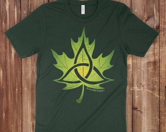 Könnte beinhalten: Ein dunkelgrünes T-Shirt mit einem grünen Ahornblatt-Design, das einen Triquetra-Knoten zeigt. Der Text "RambleTree" und "Triquetra Sugar Maple (Acer saccharum) Original artwork ©2014 Reagh Greenteaf Jr." ist auf dem Shirt aufgedruckt.