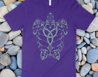 Könnte beinhalten: Ein violettes Kurzarm-T-Shirt mit einer hellgrünen Grafik einer Meeresschildkröte, die komplexe, geschwungene Muster auf ihrem Panzer und ihren Flossen aufweist. Der Schriftzug "RambleTree" ist in kleinen Buchstaben nahe der rechten Flosse gedruckt.