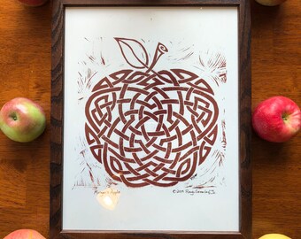May include: A framed print of a red apple with a Celtic knot design. The print is on white paper and has the text "Morgan's Apple" and "©2019 Rony Greenlay Jr."