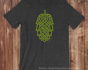 Könnte beinhalten: Ein anthrazitfarbenes Kurzarm-T-Shirt mit einer lindgrünen Grafik eines Hopfenzapfens, der mit komplizierten keltischen Knotenmustern gestaltet ist. Der Text Knotty Hop (Humulus lupulus) Original artwork ©2016 Reagh Greenleaf Jr. ist unten aufgedruckt.