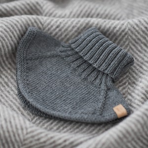 May include: A gray knitted turtleneck collar with a ribbed texture. The collar is folded and placed on a striped gray and white fabric.