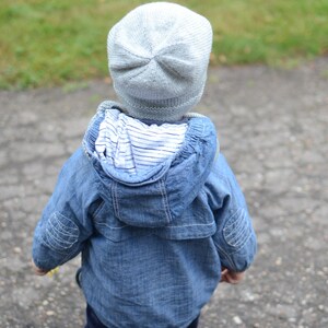 May include: A child wearing a blue denim jacket with a white striped lining and a light gray knitted hat.