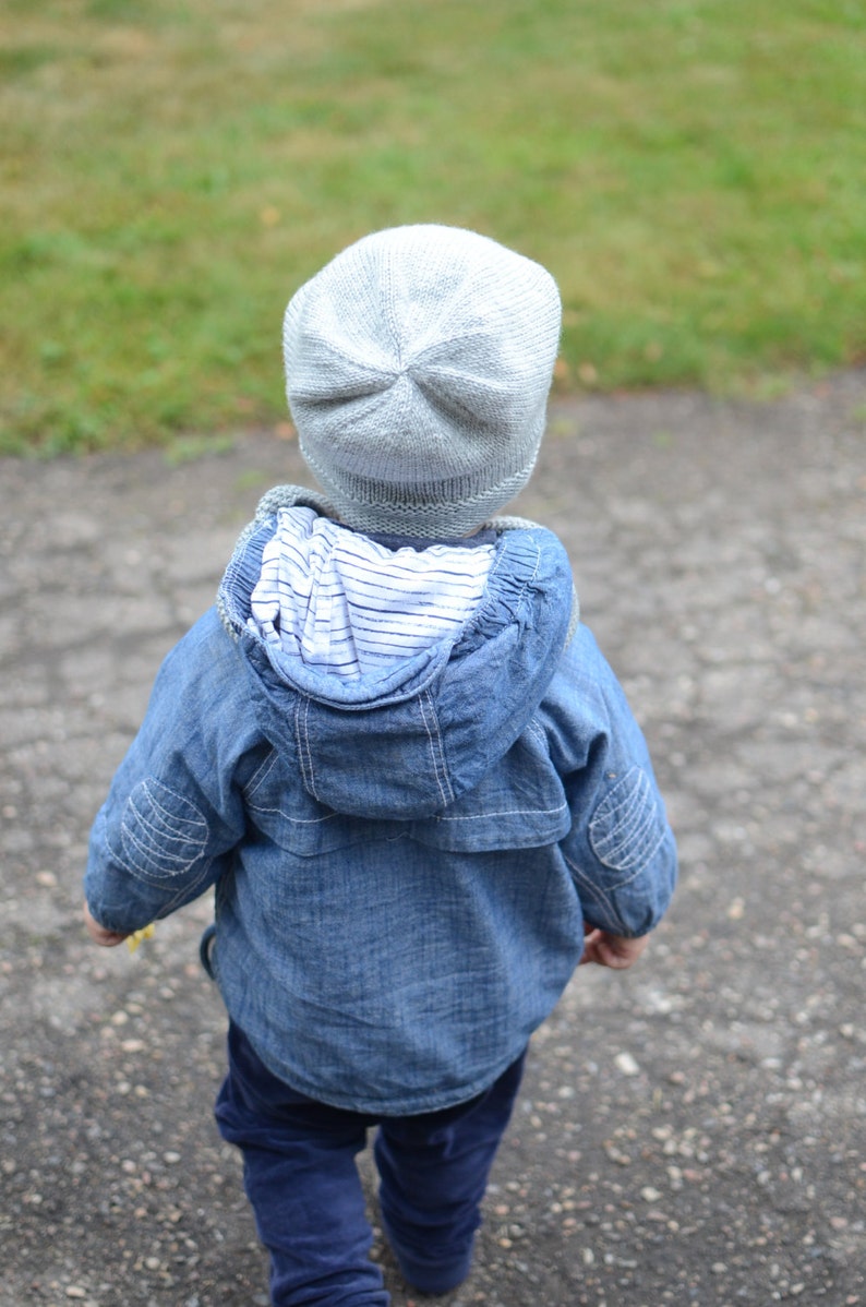 May include: A child wearing a blue denim jacket with a white striped lining and a light gray knitted hat.