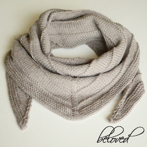 May include: A gray knitted scarf with a triangular shape and a long tail. The scarf is folded in half and the tail is hanging down.