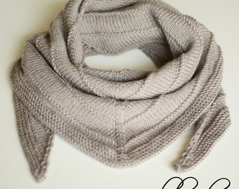 Könnte beinhalten: Ein grauer gestrickter Schal mit dreieckiger Form und einem langen Schwanz. Der Schal ist in der Mitte gefaltet und der Schwanz hängt herunter.
