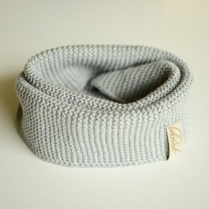 May include: A light gray knitted cowl scarf. The scarf is made of a thick, textured knit and is folded over. A small, rectangular tag with the word "beloved" is attached to the scarf.