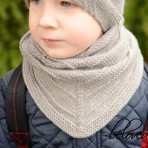 May include: A close-up of a child wearing a gray knitted scarf and hat. The scarf is folded over and has a diamond pattern. The hat is pulled down over the child's ears.