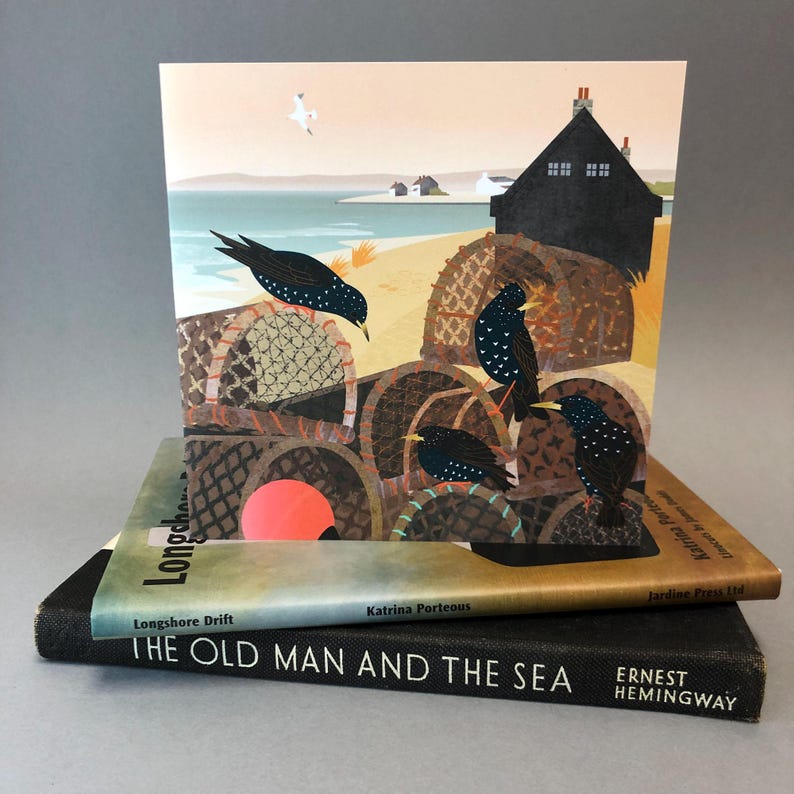 May include: A colorful illustration of a seaside scene with a black house, a beach, and a group of birds perched on top of stacked fishing baskets. The text "Longshore Drift" and "Katrina Porteous" is printed on the bottom of the card.
