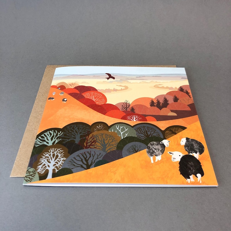 May include: A greeting card with a colorful illustration of a landscape with trees, hills, and sheep. The sky is a light blue with a bird flying in the distance. The hills are a mix of orange, red, and brown. The trees are a mix of green, brown, and gray. The sheep are white with black faces.