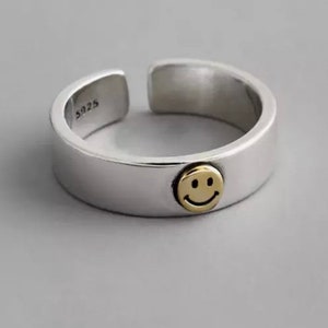 Könnte beinhalten: Ein silberner Ring mit einem goldenen Smiley-Anhänger. Der Ring ist innen mit "925" gekennzeichnet.