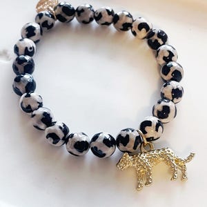 Op de afbeelding: Een armband met zwarte en witte kralen met een gouden luipaardbedel.