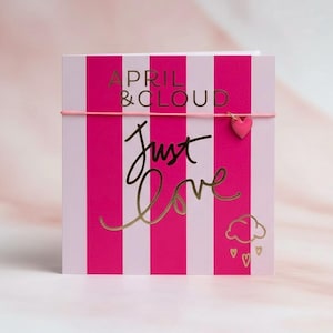 Könnte beinhalten: Eine Grußkarte mit rosa und weißen Streifen. Die Karte zeigt die Worte "APRIL & CLOUD" und "Just Love" in goldener Schrift. Ein kleiner rosa Herzanhänger hängt an einem rosa Gummiband. Eine Wolke und Herzen sind ebenfalls abgebildet.