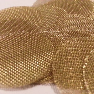 May include: Close-up of a golden mesh material with a textured, woven pattern. The material appears to be flexible and possibly used for decorative purposes or in crafting. The color is a warm, metallic gold.