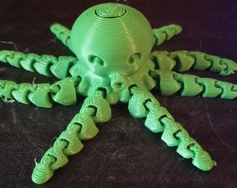 May include: A 3D-printed green octopus toy with a rounded head and segmented tentacles. The octopus has a textured surface and a playful design, perfect for children or as a decorative item. The toy is made of plastic.