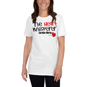 Könnte beinhalten: Weißes T-Shirt mit dem Text "The Heart Whisperer Cardiac Nurse" in Schwarz und Rot. Eine rote Herzgrafik mit einer Herzschlaglinie ist ebenfalls auf dem Shirt abgebildet. Das Shirt ist aus einem weichen Material.