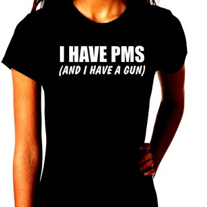 Könnte beinhalten: Schwarzes T-Shirt mit dem weißen Text "I HAVE PMS (AND I HAVE A GUN)". Das Shirt hat einen Rundhalsausschnitt und kurze Ärmel.