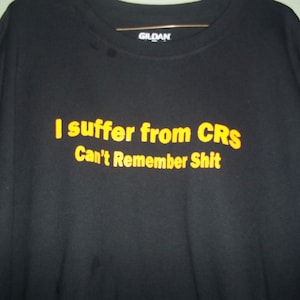 Puede incluir: Camiseta negra con el texto "I suffer from CRS Can't Remember Shit" en letras amarillas. La camiseta está hecha de un material suave y tiene cuello redondo.