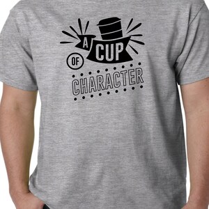 May include: A grey t-shirt featuring the black text "A Cup of Character" with a coffee cup graphic. The design is suitable for casual wear and is printed on a grey t-shirt.