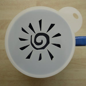 Peut inclure: Pochoir en plastique blanc avec un motif de soleil noir. Le soleil a une spirale au centre et des rayons qui s'étendent vers l'extérieur.