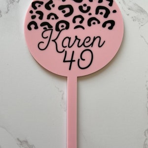 May include: Pink round cake topper with black leopard print and the text "Karen 40" in black cursive font.