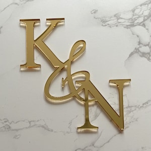 May include: Gold mirrored acrylic letters spelling "K & N" in a cursive font. The letters are attached to each other.