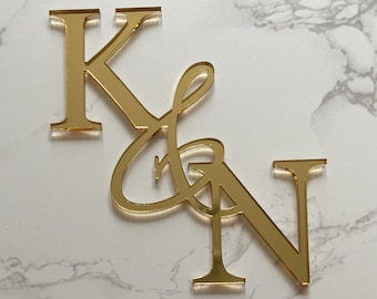 May include: Gold mirrored acrylic letters spelling "K & N" in a cursive font. The letters are attached to each other.