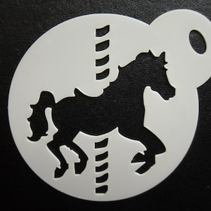 May include: White plastic stencil with a carousel horse design. The horse is depicted in motion, with a flowing mane and tail. The stencil has a circular shape and a handle. Suitable for crafts and decorative projects.