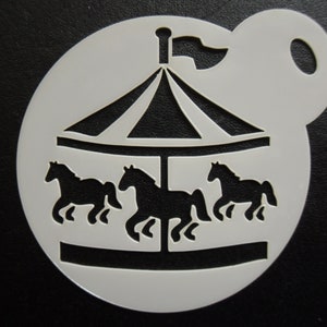 May include: A white plastic stencil with a carousel design. The carousel features three horse silhouettes, a striped roof, and a flag. The stencil is circular with a handle for ease of use, ideal for crafts.