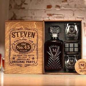 Könnte beinhalten: Ein hölzernes Geschenkset mit einer personalisierten Whiskykaraffe, zwei Gläsern und Whisky-Steinen. Die Karaffe und die Gläser sind mit einem Monogramm graviert. Die Holzkiste ist mit dem Namen "STEVEN" und dem Text "Old No. 43 Years" graviert.
