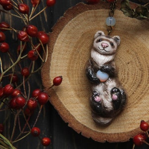 May include: A brown and white ferret figurine holding a small, white, round object. The figurine is on a wooden slice with a brown background.