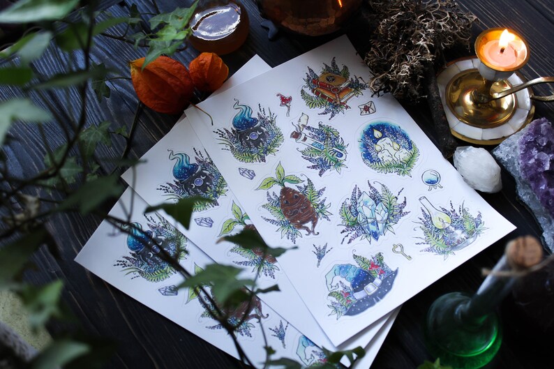 May include: Three sheets of paper with illustrations of various magical items, including a witch's hat, a book, a potion bottle, and a crystal. The illustrations are in a whimsical style with a blue, green, and purple color scheme.