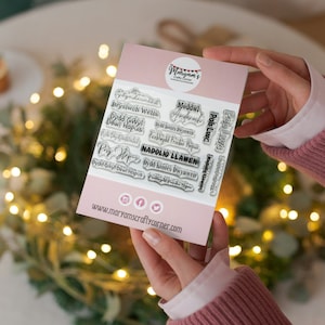 May include: A set of clear acrylic stamps with Welsh language phrases, including "Dydd Gwyl Dewi Hapus" (St. David's Day Happy) and "Nadolig Llawen" (Merry Christmas). The stamps are arranged on a pink card with the website address "www.maryamscraftycorner.com".