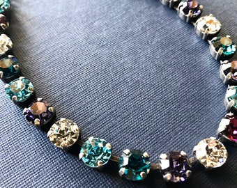 May include: A silver chain necklace with a variety of colored round crystals. The crystals are in shades of blue, purple, and white.