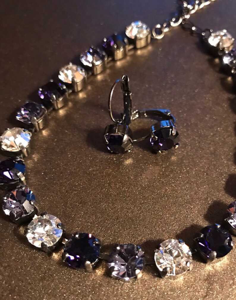 May include: A silver necklace and earrings set with a gradient of clear and dark purple crystals.