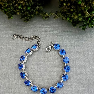 Puede incluir: Un brazalete de plata con cierre de cadena y una fila de piedras de cristal azul.