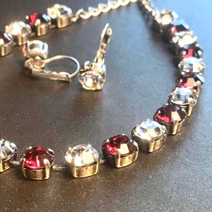 May include: A silver chain necklace with alternating clear and burgundy red crystal stones. The necklace is paired with a matching pair of clip-on earrings.