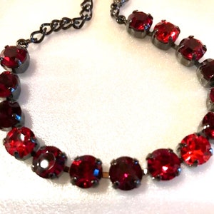 May include: A red crystal bracelet with a black chain and clasp. The bracelet is made of round, faceted crystals.