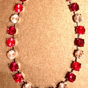May include: A silver necklace with alternating clear and red round rhinestones.