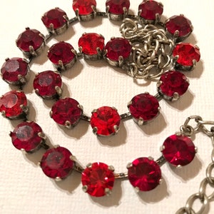 May include: A red rhinestone necklace with a silver chain. The necklace is made of round red rhinestones that are set in silver.