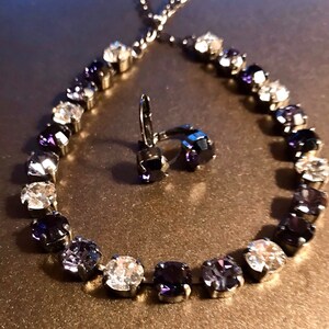 May include: A silver necklace and earrings set with a gradient of clear and dark purple crystals.