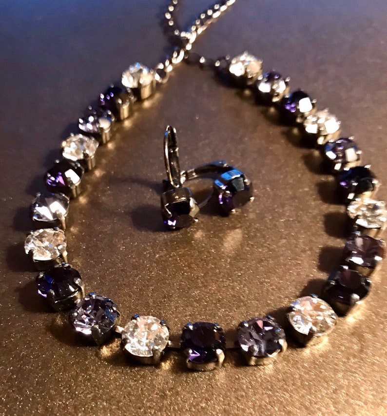 May include: A silver necklace and earrings set with a gradient of clear and dark purple crystals.