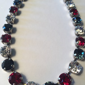 May include: A silver necklace with alternating red, black, clear, and green round stones.