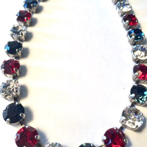 May include: A silver chain necklace with alternating red, white, and blue round crystals. The necklace is made of metal and has a simple design.