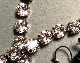 May include: A silver chain necklace with clear crystal rhinestones and black metal clasp closures.