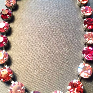 Puede incluir: Un collar de cadena de plata con cristales redondos rojos y rosados. Los cristales están engastados en engastes de plata y están dispuestos en un patrón graduado, con los cristales más grandes en el centro y los cristales más pequeños en los extremos.