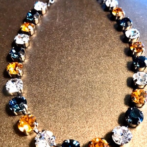 Puede incluir: Un collar de cadena de plata con un patrón degradado de piedras de cristal transparentes, ámbar y azules.